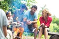 Happy family sitting with woman while roasting marshmallows over burning campfire at park Royalty Free Stock Photo