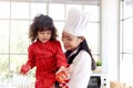 Happy family, smiling beautiful Asian mother wears cute red heart apron and chef hat holds daughter while little girl holds apple Royalty Free Stock Photo
