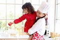 Happy family, smiling beautiful Asian mother wears cute red heart apron and chef hat holds daughter while little girl holds apple Royalty Free Stock Photo