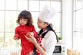 Happy family, smiling beautiful Asian mother wears cute red heart apron and chef hat holds daughter while little girl holds apple Royalty Free Stock Photo