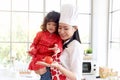 Happy family, smiling beautiful Asian mother wears cute red heart apron and chef hat holds daughter while little girl holds apple Royalty Free Stock Photo