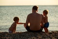 Happy family spend time together sitting on a pebble beach at sunset. Royalty Free Stock Photo