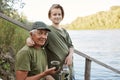 Happy family spending time together outdoor. Father and son sitting on wooden placing near water, drinking hot beverage, looking