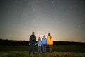 Happy family standing in night field looking at dark sky with many bright stars. Parents and children observing meteor shower Royalty Free Stock Photo