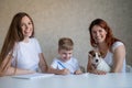 Happy family stays at home. Two women help the boy do school homework. Lesbian couple sitting at the table with their Royalty Free Stock Photo