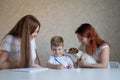 Happy family stays at home. Two women help the boy do school homework. Lesbian couple sitting at the table with their Royalty Free Stock Photo