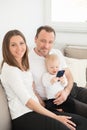 Happy family of three is enjoying at home. Parents and their beautiful baby girl sitting on the sofa and looking at the camera. Royalty Free Stock Photo