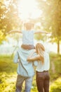 Happy family of three persons walking the grass in the park on sunset. happy daughter flying on father back Royalty Free Stock Photo