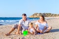 Happy family of three - pregnant mother, father and daughter having fun, playing with sand and shells on the beach. Family vacatio Royalty Free Stock Photo