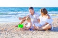 Happy family of three - pregnant mother, father and daughter having fun, playing with sand and shells on the beach. Family vacatio Royalty Free Stock Photo