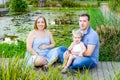 Portraits of happy family of three - pregnant wife, father and daughter having fun near pond with water lilies in the park. Family Royalty Free Stock Photo