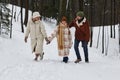 Happy family of three in winterwear walking along forest road covered with snow Royalty Free Stock Photo