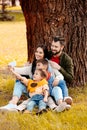 Happy family with two children sitting together on grass in park and taking a selfie Royalty Free Stock Photo