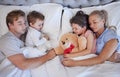 Happy family with two children sleeping together in their parents bed, from above. Loving parents cuddling two little Royalty Free Stock Photo