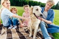 happy family with two children stroking dog while sitting on plaid Royalty Free Stock Photo