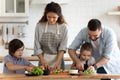Happy family with two little kids cooking salad, cutting vegetables Royalty Free Stock Photo