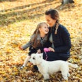 Happy family walking with dog in autumn park. Young mother and daughter with white dog having fun in fallen leaves. Autumn holiday Royalty Free Stock Photo