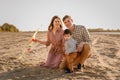 Happy family walking on sandy beach of river. Father, mother holding baby son on hands and playing with kite Royalty Free Stock Photo