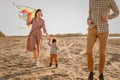 Happy family walking on sandy beach of river. Father, mother holding baby son on hands and playing with kite Royalty Free Stock Photo