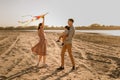 Happy family walking on sandy beach of river. Father, mother holding baby son on hands and playing with kite Royalty Free Stock Photo