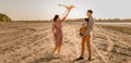 Happy family walking on sandy beach of river. Father, mother holding baby son on hands and playing with kite Royalty Free Stock Photo