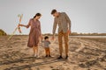 Happy family walking on sandy beach of river. Father, mother holding baby son on hands and playing with kite Royalty Free Stock Photo