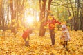 happy family walking in sunny park and throws orange maple leaves. mother with kids enjoying autumn weather outdoors Royalty Free Stock Photo