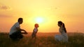 Happy family walks in park at sunset. Mom, dad and baby. Little daughter goes from mom to dad, hugs and kisses her Royalty Free Stock Photo