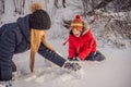 Happy family in warm clothing. Smiling mother and son making a snowman outdoor. The concept of winter activities Royalty Free Stock Photo