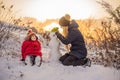 Happy family in warm clothing. Smiling mother and son making a snowman outdoor. The concept of winter activities Royalty Free Stock Photo