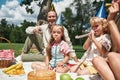 Happy family wearing party hats, celebrating kids birthday in the park on a summer day. Children having fun, blowing Royalty Free Stock Photo