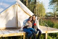 Happy family wraps blanket over themselves while sitting near canvas tent in the woods Royalty Free Stock Photo