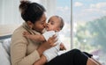 Happy family young African mother sitting holding and kissing a cute daughter baby on the bed at home