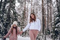 Happy family young mother and little cute girl in pink warm outwear walking having fun in snowy white cold winter forest outdoors Royalty Free Stock Photo