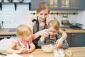 Happy family young mother and two little daughters preparing dough for pancakes or cookies together in the kitchen Royalty Free Stock Photo