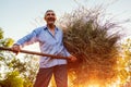 Happy farmer man gathers hay with pitchfork at sunset in countryside