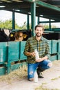 happy farmer squatting near stable with cows and holding bottle