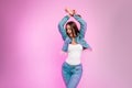 Happy fashion model joyful young woman in denim jacket in jeans in a t-shirt is standing and smiling near modern pink wall in the Royalty Free Stock Photo