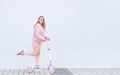 Girl in pink clothes rides on a pink kick scooter, looks into the camera and smiles, isolated on a white background Royalty Free Stock Photo