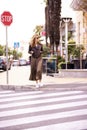 Happy fashionable woman walking on pedestrian crossing in the city