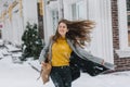 Happy fashionable young woman enjoying snowfall weather on steet in city. Long brunette hair, snowing time, excited