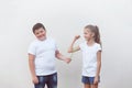 Happy fat little caucasian boy in white shirt measuring thin small beautiful girl muscle with tape