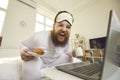 Happy fat man in pajamas sitting on bed in the morning, enjoying breakfast and laughing Royalty Free Stock Photo