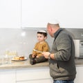 Happy father with child lighting candles on traditional menorah at kitchen, celebrating Hanukkah at home.