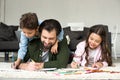 happy father with cute children lying on carpet and drawing with colored