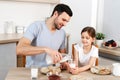 Happy father and daughter have breakfast at kitchen, eats delicious pancakes with jam, drink milk, enjoys delicious food