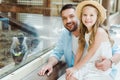 happy father and daughter looking at camera near monkey while sitting near window in zoo. Royalty Free Stock Photo