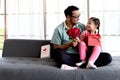 Happy Father Day, cute little girl sits on daddy lap on sofa in living room, giving present gift box flower and card to dad for Royalty Free Stock Photo