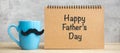 Happy Father day with paper notepad, Blue coffee cup or tea mug and Black mustache decor on table. International men day and Royalty Free Stock Photo