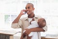 Happy father feeding his baby boy a bottle while on the phone Royalty Free Stock Photo